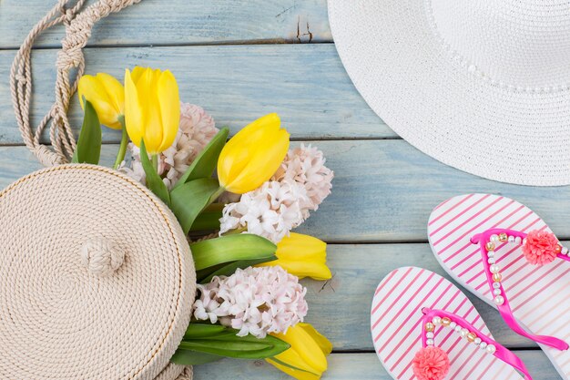 tongs, chapeau de plage, sac rond en osier et un bouquet de tulipes et jacinthes