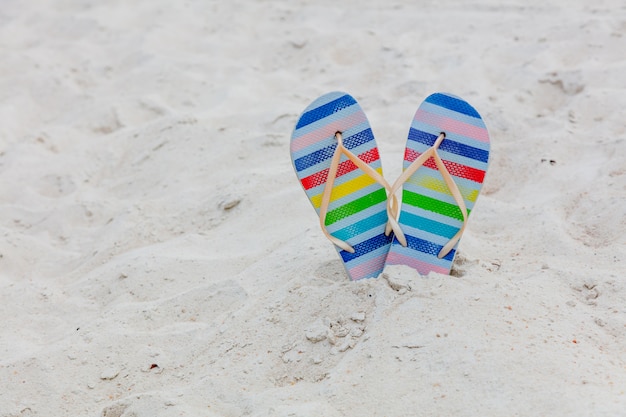 Tongs chaussures à rayures de couleur sur un sable blanc.