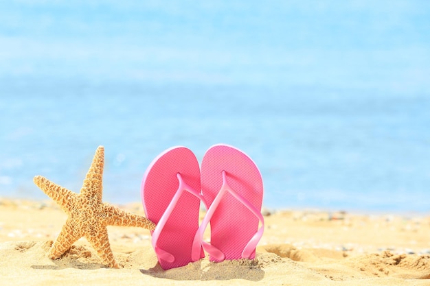 Tongs colorées et étoiles de mer sur le sable au bord de la mer Concept de vacances