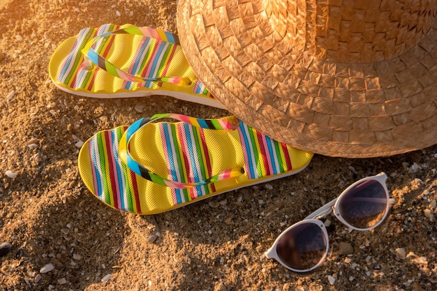 Tongs et lunettes de soleil chapeau de plage sur fond de sable l'été chaud de la station balnéaire exotique vous appelle