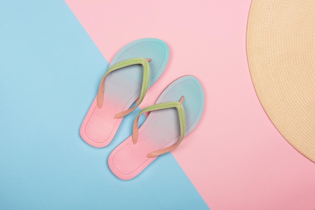 Tongs de plage élégantes et chapeau de soleil sur la vue de dessus de fond pastel rose et bleu