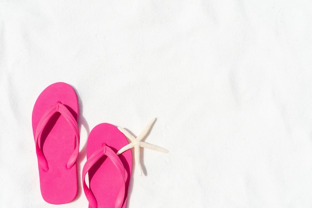 Tongs rose sur fond de plage de sable blanc avec étoile de mer.