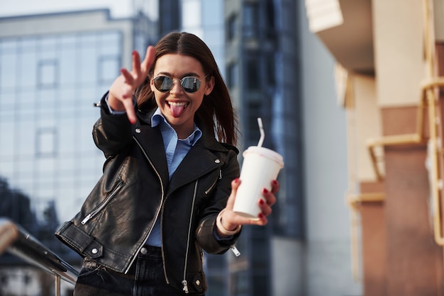 Tongue out, s'amuser. Jeune belle fille dans des vêtements chauds se promène dans la ville à son heure du week-end