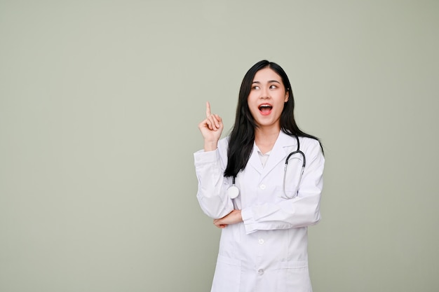 Étonné femme médecin asiatique debout sur fond gris isolé pointant le doigt vers le haut