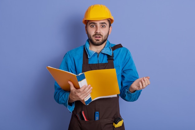 Étonné jeune constructeur choqué en casque jaune debout avec la bouche ouverte et être très surpris