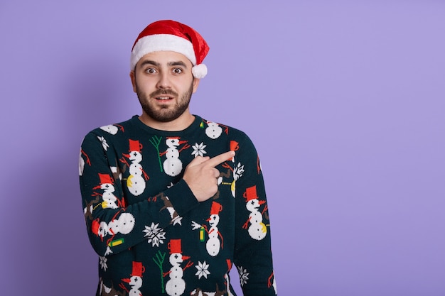 Étonné jeune homme de race blanche Santa en pull et chapeau de Noël