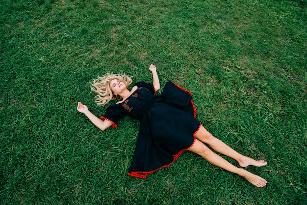 Top biew de belle femme blonde en robe noire allongée sur l'herbe verte