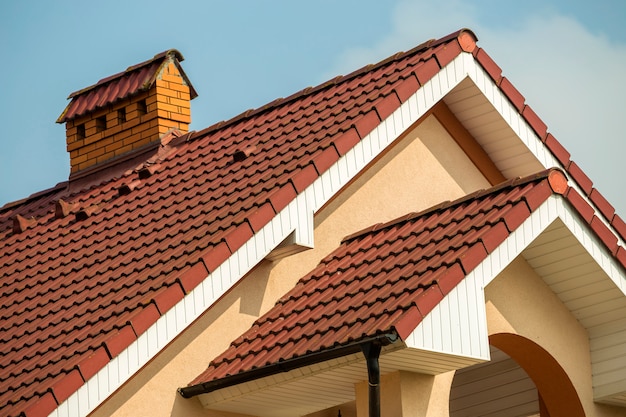 Top détail du grand chalet résidentiel cher et moderne avec toit en bardeaux raides, cheminée en brique, murs en stuc sur fond de ciel bleu. Construction, toiture professionnelle et concept d'investissement.