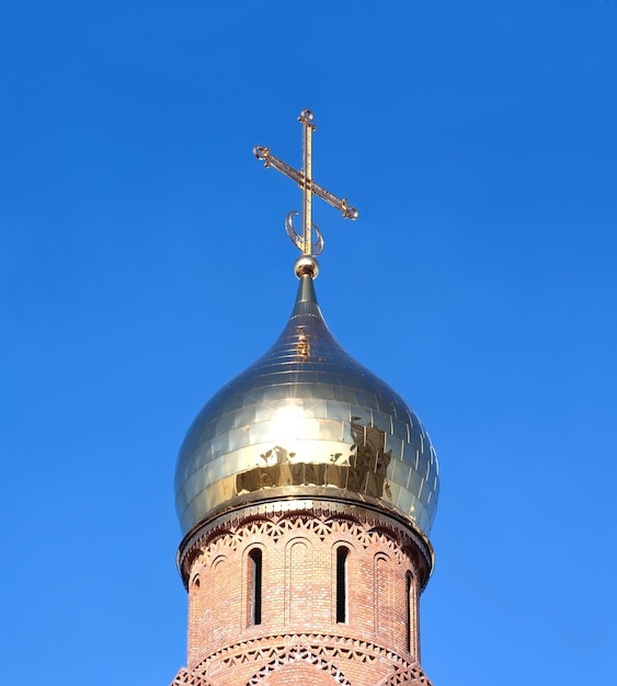 Top d'une église chrétienne en briques rouges avec une coupole dorée sur un ciel bleu clair en gros plan