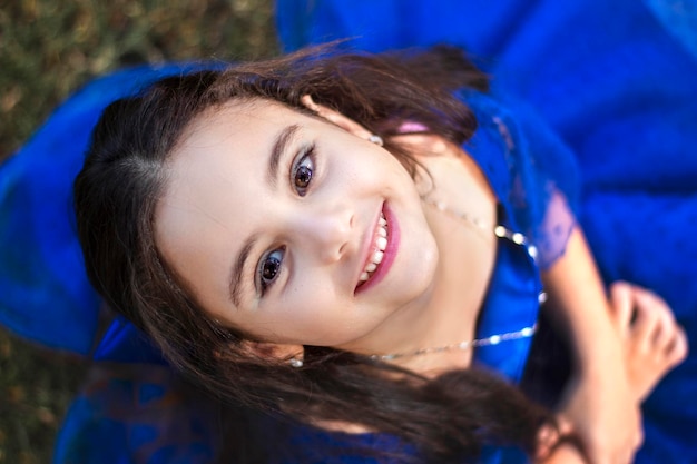 Top shot du visage d'une belle petite fille vêtue d'une robe bleu marine regardant la caméra en position assise