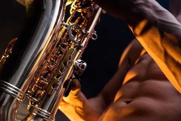 Torse nu d'homme musclé jouant au saxophone avec fond coloré fumé