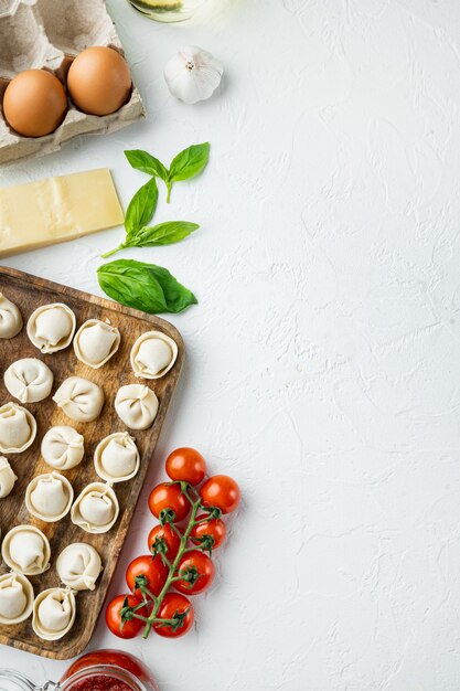 Tortellini italien avec des feuilles de ricotta fraîches et des tomates dans un plateau en bois, sur fond blanc, vue de dessus à plat,