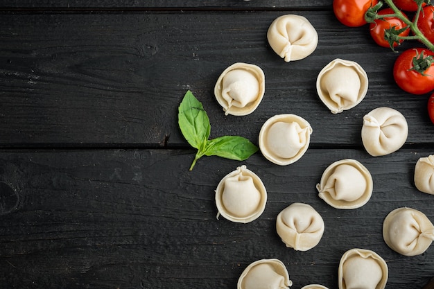 Tortellini italien avec des feuilles de ricotta fraîches et des tomates, sur fond de table en bois noir, vue de dessus à plat, avec copyspace et espace pour le texte