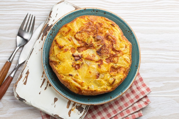 Tortilla espagnole maison - omelette avec pommes de terre sur plaque sur fond rustique en bois blanc vue de dessus. Plat traditionnel d'Espagne Tortilla de patatas pour le déjeuner ou le goûter, frais généraux