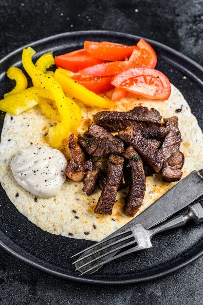 Tortilla avec steak de viande de boeuf et salade fraîche sur une assiette rustique.