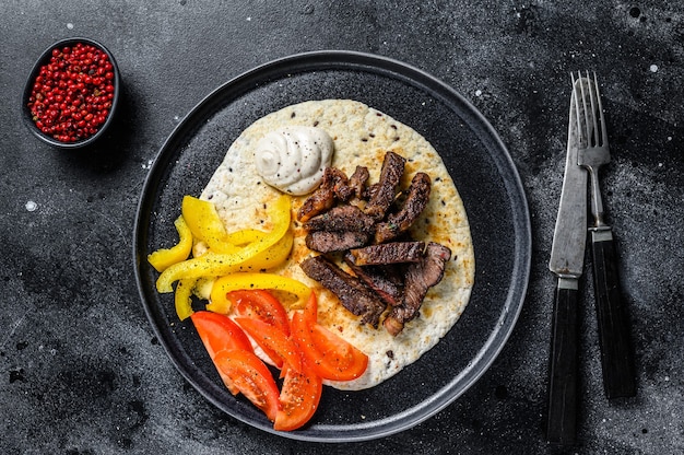 Tortilla avec steak de viande de boeuf et salade fraîche sur une assiette rustique.