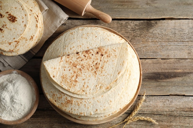 Des tortillas maison savoureuses, du rouleau à farine et des pointes sur une table en bois à plat, espace pour le texte.