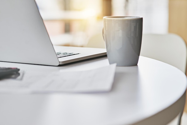 Tôt le matin au bureau Gros plan d'un ordinateur portable et d'une tasse de café assis sur un bureau