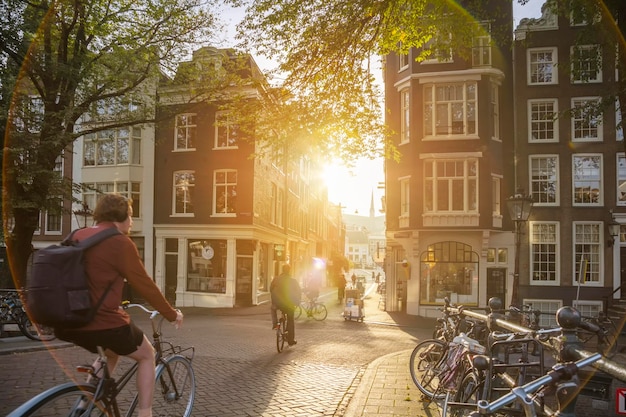 Tôt le matin, les gens font du vélo dans l'ancienne ville européenne d'Amsterdam Lumière du soleil et silhouettes belles maisons du centre-villexAvec une véritable lumière parasite Image artistiquexAAmsterdam Hollande Pays-Bas Europe