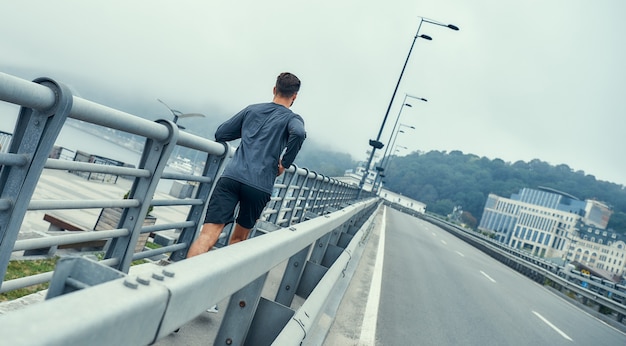 Tôt le matin, vue arrière d'un homme jeune et en bonne santé en vêtements de sport faisant du jogging sur le