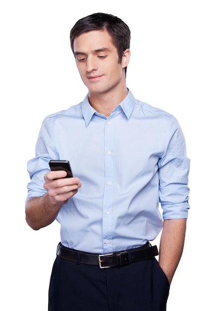 Toujours en contact. Beau jeune homme en tenue de soirée tenant un téléphone portable et souriant en se tenant debout isolé sur blanc