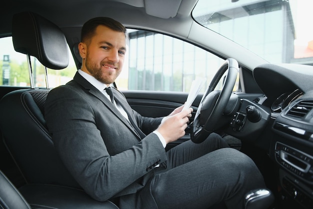 Toujours pressé Beau jeune homme en costume complet souriant tout en conduisant une voiture