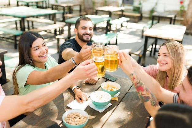 Toujours s'amuser entre amis. Jeunes femmes et hommes enthousiastes portant un toast avec des bières froides et célébrant leurs retrouvailles