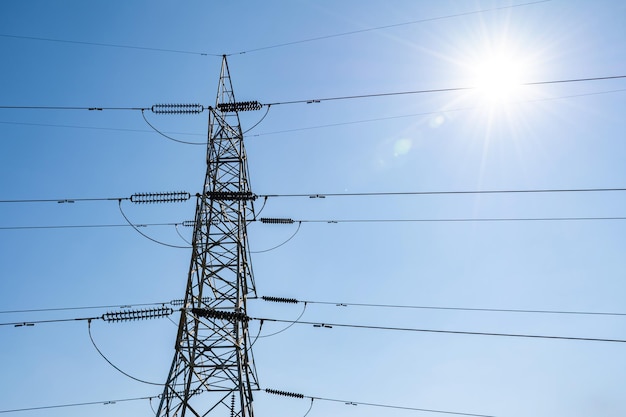 Tour en acier d'énergie électrique haute tension contre l'éclat du soleil et le ciel bleu clair.