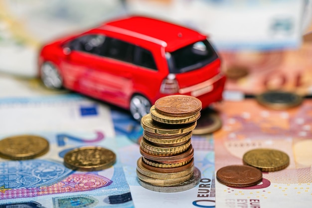 Tour avec pièces en euros sur fond de billets de banque et concept d'assurance et de prêt de voiture jouet rouge