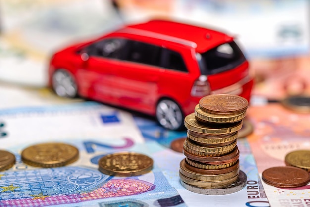 Tour avec pièces en euros sur fond de billets de banque et concept d'assurance et de prêt de voiture jouet rouge