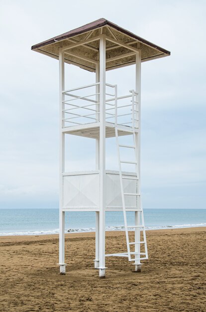 Tour de sauveteur vide et drapeau de tempête rouge sur la plage par temps nuageux. Image verticale