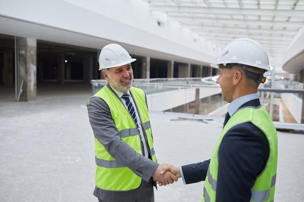 Tour de taille portrait of smiling mature businessman serrant la main avec partenaire après accord d'investissement au chantier de construction,