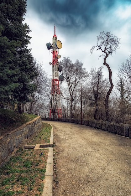 Tour de télévision à côté de la route goudronnée, ciel dramatique, ancienne route de campagne de la montagne forestière avec clôture en pierre.