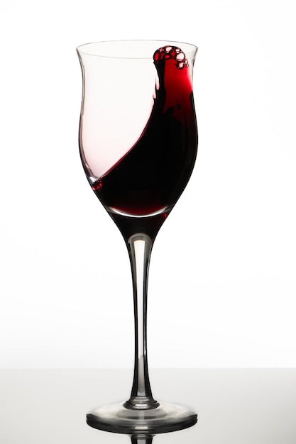 Photo tourbillon ou mouvement de liquide dans un verre de vin rouge. fond blanc, orientation verticale. concept de mouvement, d'élégance, de goût.