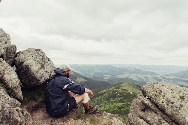 Tourisme, montagnes, mode de vie, nature, concept de personnes- Jeune homme debout au sommet d'une falaise dans les montagnes d'été au coucher du soleil et profitant de la vue sur la nature