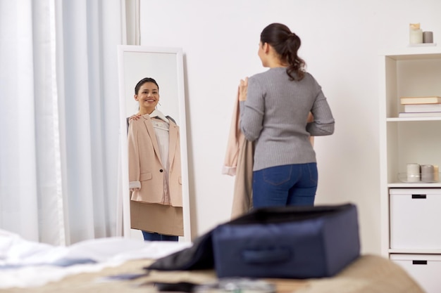 tourisme, voyage d'affaires, concept de personnes et de bagages - jeune femme heureuse emballant un sac de voyage à la maison ou dans une chambre d'hôtel