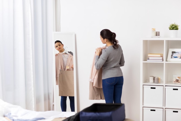 tourisme, voyage d'affaires, concept de personnes et de bagages - jeune femme heureuse emballant un sac de voyage à la maison ou dans une chambre d'hôtel