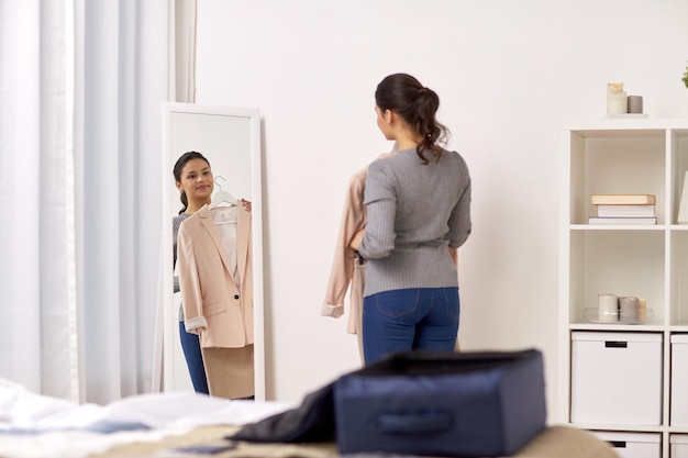 tourisme, voyage d'affaires, personnes et concept de bagages - jeune femme heureuse emballant un sac de voyage à la maison ou dans une chambre d'hôtel