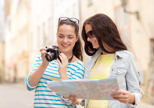 tourisme, voyage, loisirs, vacances et concept d'amitié - deux adolescentes souriantes avec carte et appareil photo à l'extérieur