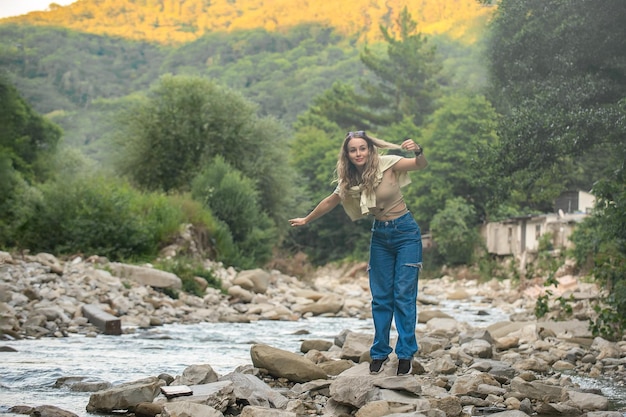 une touriste aime la vie près d'une rivière de montagne sur les rochers, en arrière-plan elle a des montagnes