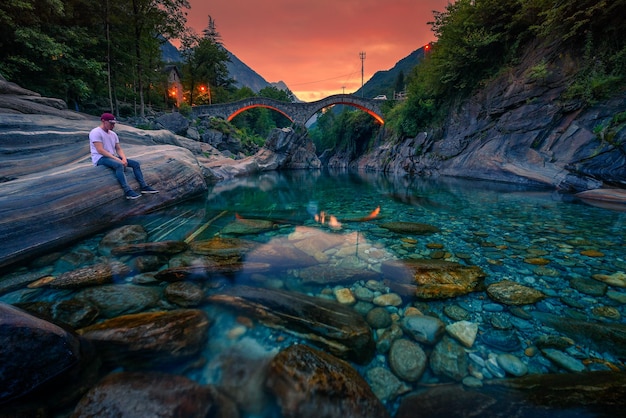 Le touriste apprécie le coucher du soleil sur une rivière près d'un pont de pierre à lavertezzo suisse