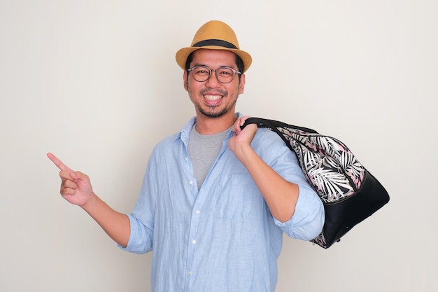 Un touriste asiatique apporte un sac de transport à main souriant heureux et pointant vers le côté droit