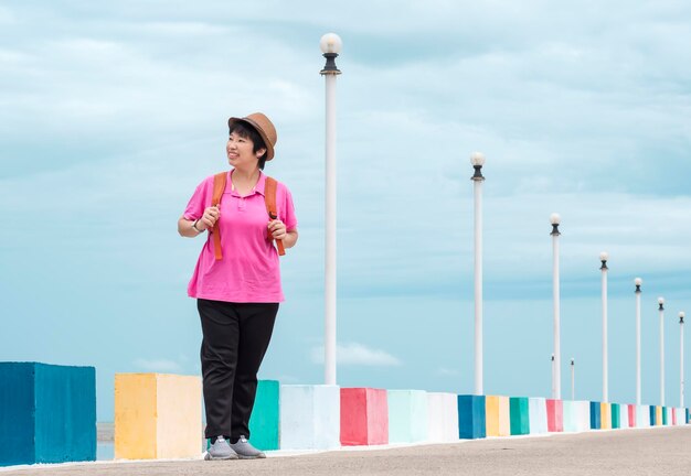 Une touriste asiatique souriante regardant de côté tout en se tenant sur le pont au point de vue de la mer