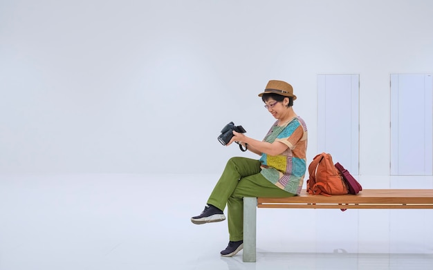 Touriste asiatique vérifiant la photo sur l'appareil photo tout en étant assis sur un banc en bois dans la zone de la station de métro