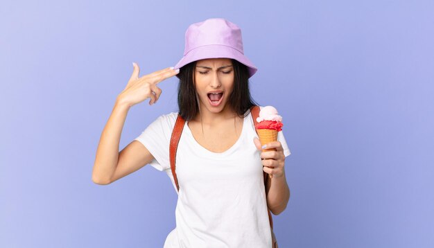 Touriste assez hispanique à l'air malheureux et stressé, geste de suicide faisant un signe d'arme à feu et tenant une glace