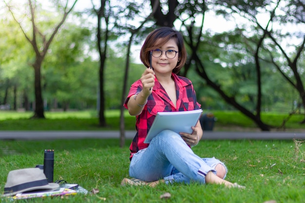 Touriste assis sur l&#39;herbe et pense à dessiner dans un parc verdoyant