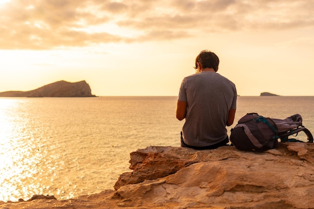 Un touriste assis en regardant le coucher du soleil à la plage de Cala Comte sur l'île d'Ibiza Baléares