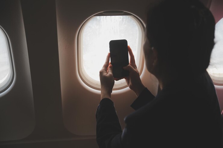 Une touriste blonde vérifiant les notifications entrantes sur son smartphone assise sur le siège de l'avion avec un netbook Une jeune femme d'affaires partage des médias depuis son téléphone sur son ordinateur portable pendant le vol en avion