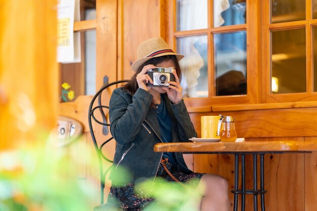 Une touriste avec un chapeau et un appareil photo buvant du thé sur une terrasse de café prenant des photos de ses vacances