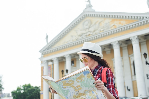 Photo la touriste avec chapeau et lunettes de soleil tenant une carte et la regardant contre le bâtiment avec des colonnes